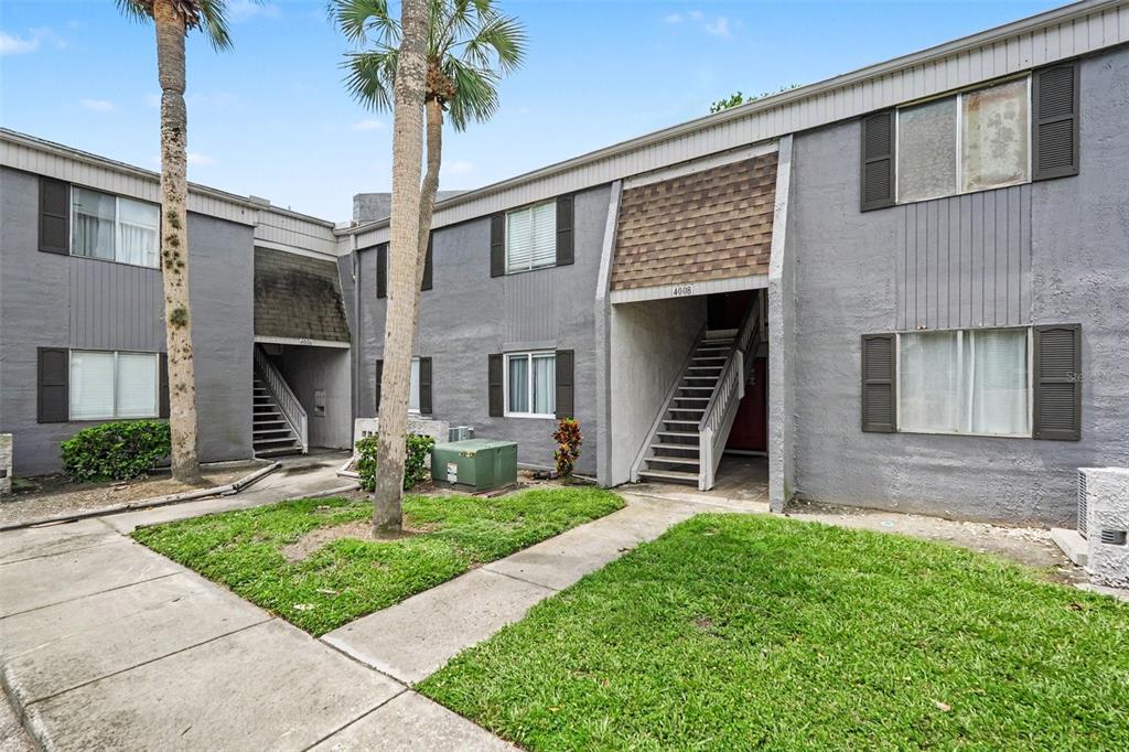 A two-story gray apartment building features exterior staircases and palm trees in the front yard — 4008 CORTEZ DRIVE UNIT B, TAMPA, FL