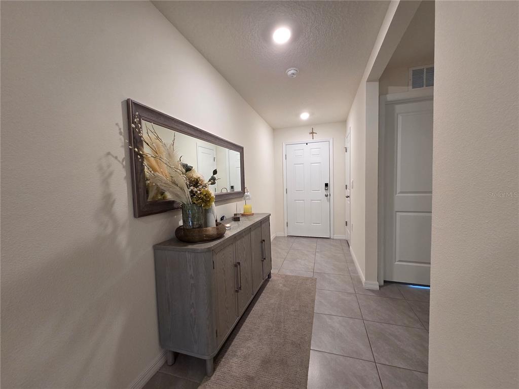 A hallway features a gray wooden console table, a large wall mirror, and tiled flooring — 4446 BAYRIDGE COURT, SPRING HILL, FL
