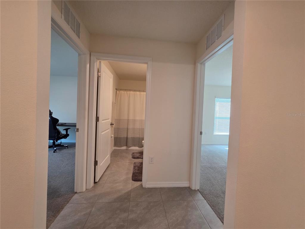 A hallway with tile flooring leads to a bathroom and two carpeted rooms — 4446 BAYRIDGE COURT, SPRING HILL, FL