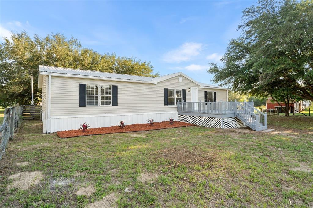 A single-story manufactured home with light siding, a metal roof, and a wooden deck — 11330 NE 84TH COURT, BRONSON, FL