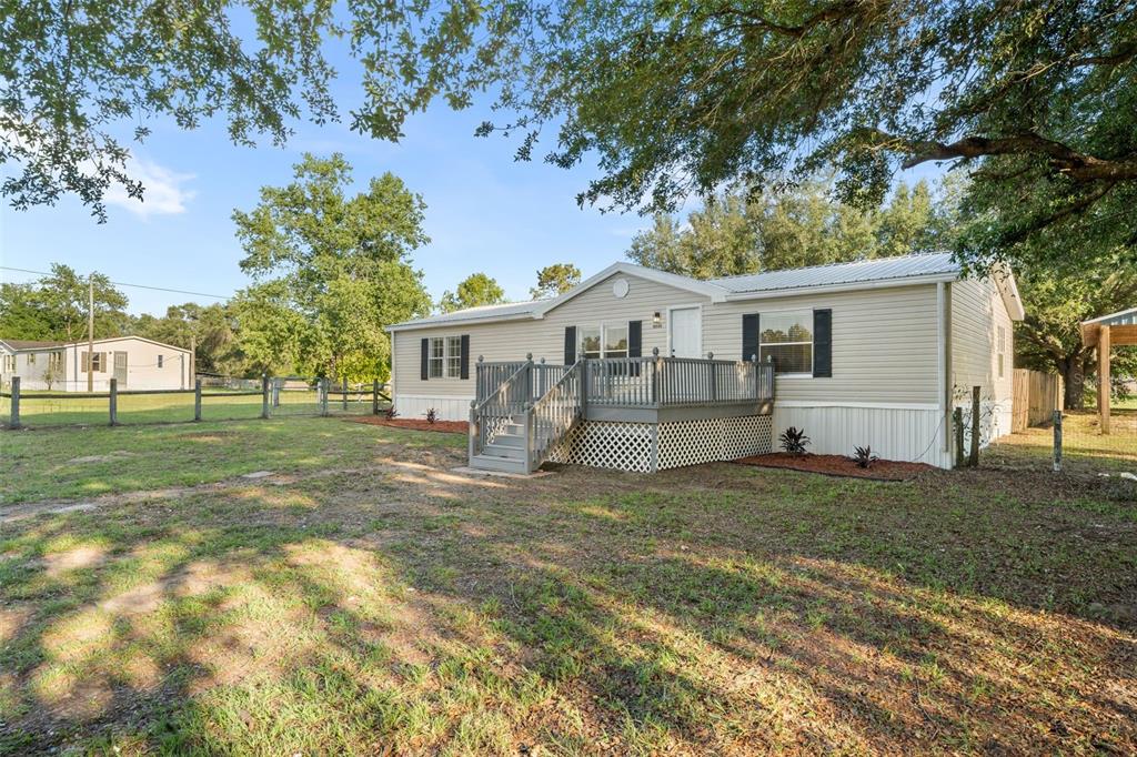 A single-story manufactured home with light siding and a gray wooden deck sits on grass — 11330 NE 84TH COURT, BRONSON, FL