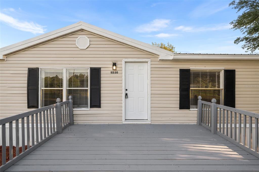 A beige manufactured home features a gray wooden deck and a white front door — 11330 NE 84TH COURT, BRONSON, FL