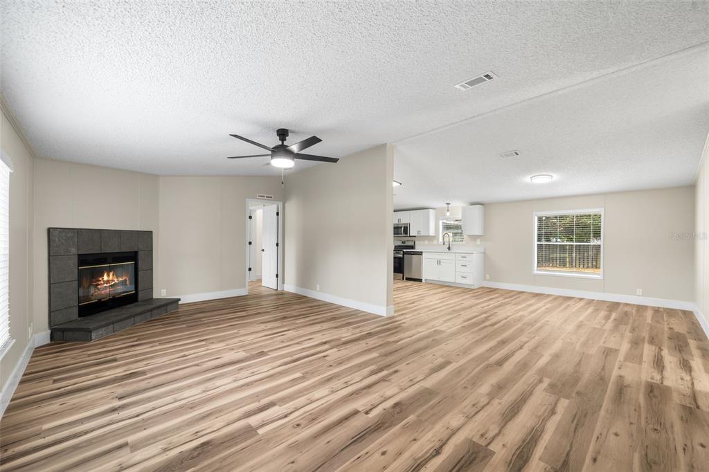 A living room with wood-look flooring and a fireplace opens into a white kitchen — 11330 NE 84TH COURT, BRONSON, FL