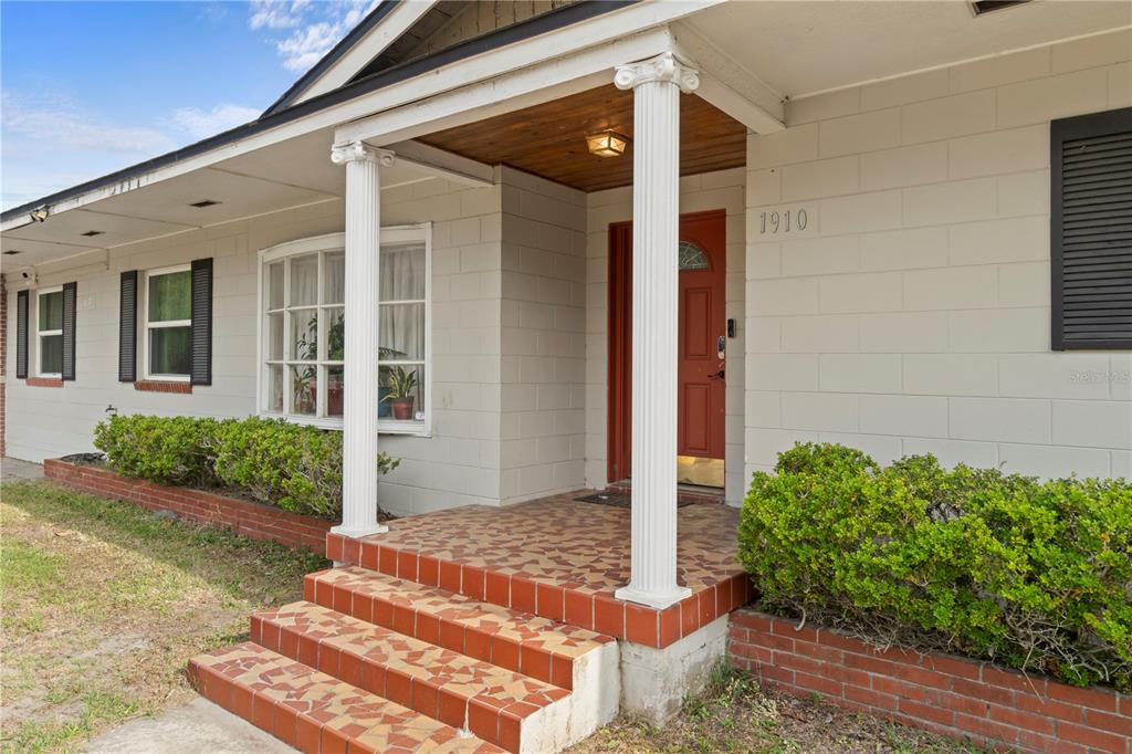 A house exterior features a tiled porch, two white columns, and a red front door — 1910 NW 14TH STREET, OCALA, FL