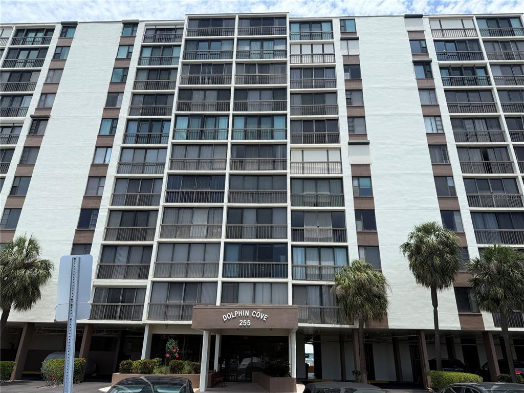 A low-angle view of the exterior of a multi-story apartment building named Dolphin Cove — 255 DOLPHIN POINT UNIT 2, CLEARWATER BEACH, FL