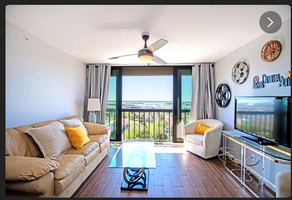 A living room with a tan sofa, glass coffee table, and balcony overlooking the water — 255 DOLPHIN POINT UNIT 2, CLEARWATER BEACH, FL