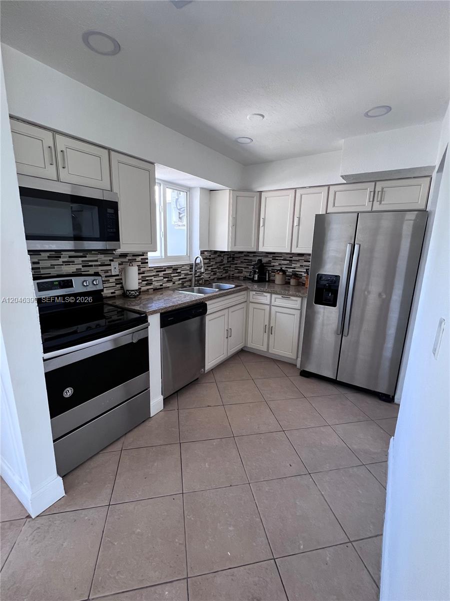 A kitchen features stainless steel appliances, off-white cabinetry, a tiled backsplash, and diagonal floor tiles — 600 N 70th Ter, Hollywood FL 33024, HOLLYWOOD, FL