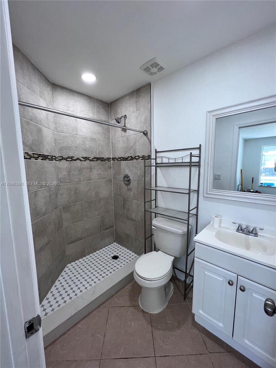 A bathroom features a tiled walk-in shower, a toilet with a shelving unit, and vanity — 600 N 70th Ter, Hollywood FL 33024, HOLLYWOOD, FL