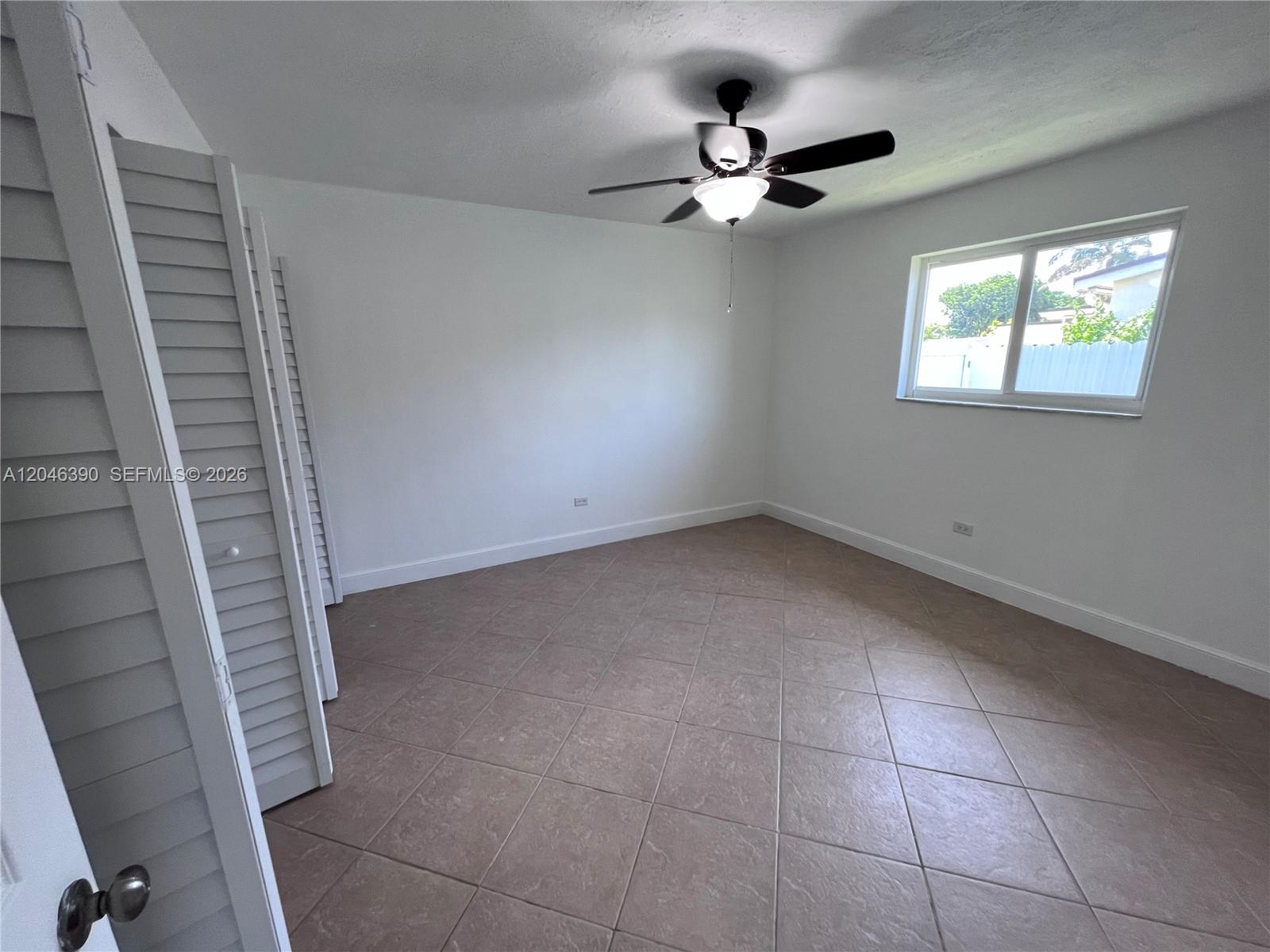 An empty bedroom features white walls, tile flooring, a ceiling fan, and louvered closet doors — 600 N 70th Ter, Hollywood FL 33024, HOLLYWOOD, FL