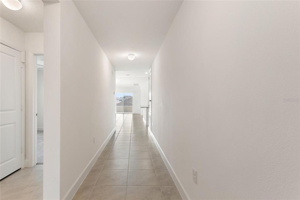 A long, tiled hallway leads toward a bright living area with a sliding glass door — 9239 WESTSIDE HILLS DR, DAVENPORT, FL