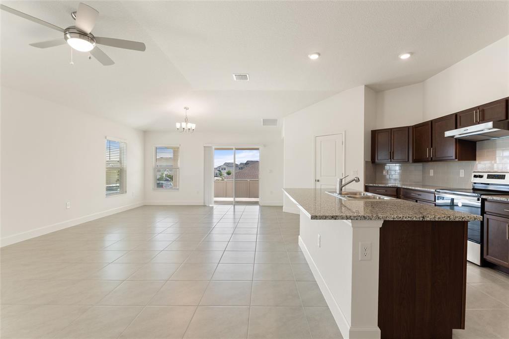 A kitchen with dark cabinets and granite countertops opens into a spacious, tiled living area — 9239 WESTSIDE HILLS DR, DAVENPORT, FL