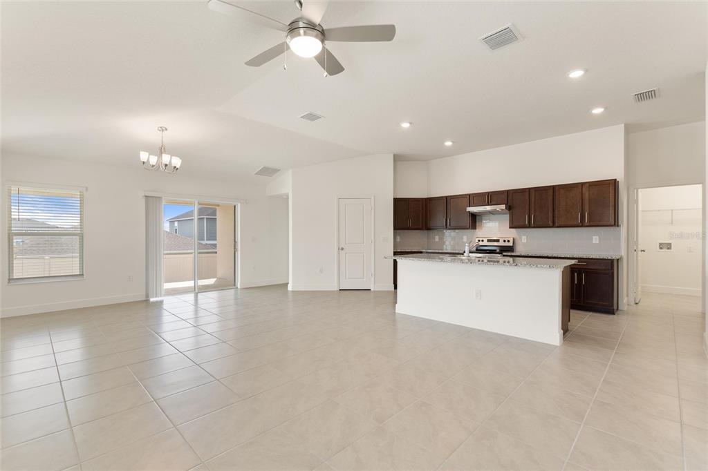 An open-concept kitchen and living area with tile flooring, dark wood cabinets, and granite countertops — 9239 WESTSIDE HILLS DR, DAVENPORT, FL