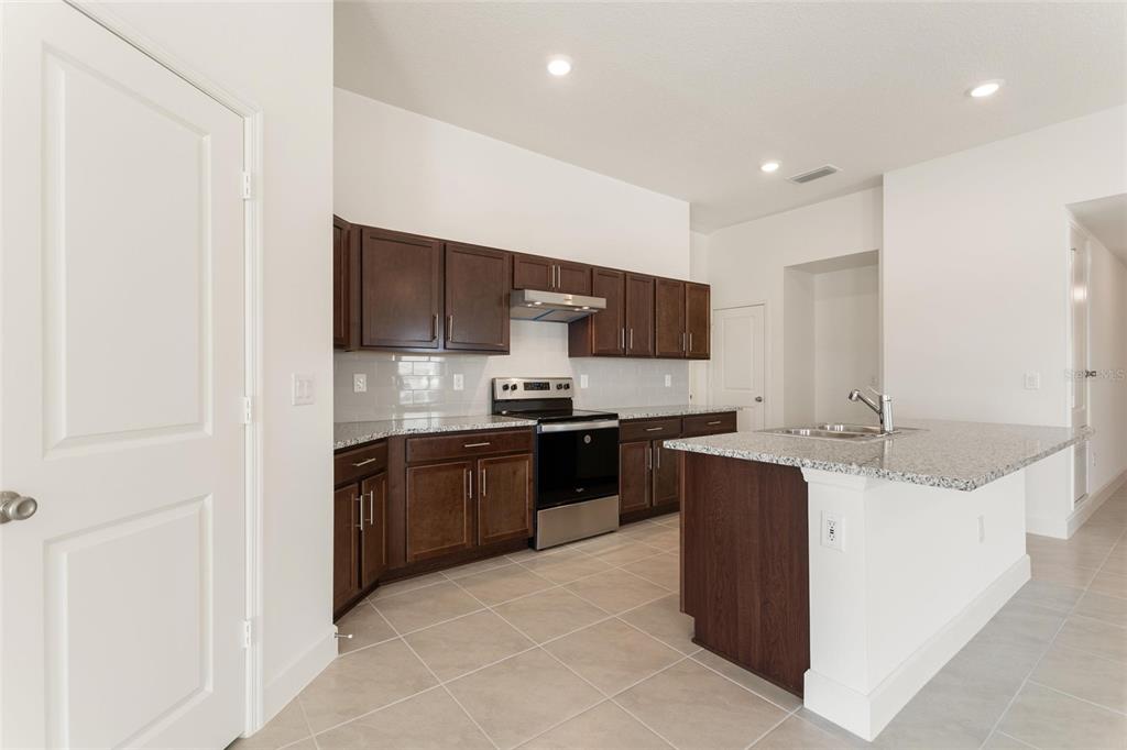 A kitchen features dark wood cabinets, granite countertops, stainless steel appliances, and a central island — 9239 WESTSIDE HILLS DR, DAVENPORT, FL