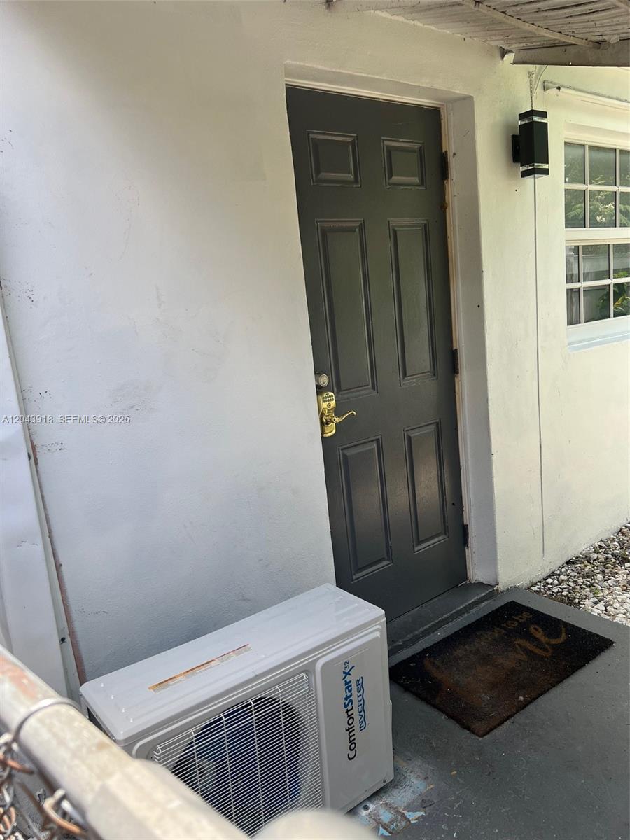 A white exterior wall features a dark gray door, a window, and an outdoor AC unit — 0 East Dr. # 0, North Miami Beach FL 33162, NORTH MIAMI BEACH, FL