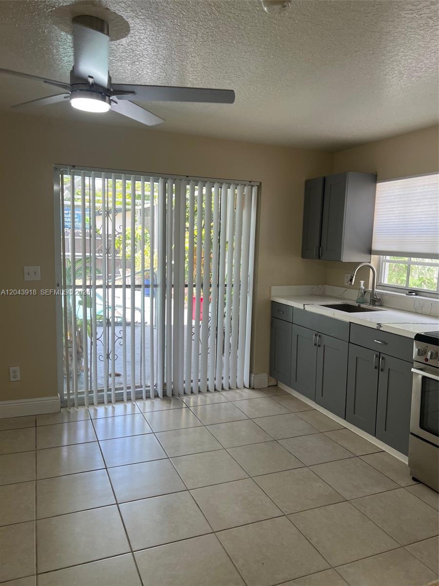 A kitchen with gray cabinets, white countertops, tile flooring, and a sliding glass door — 0 East Dr. # 0, North Miami Beach FL 33162, NORTH MIAMI BEACH, FL