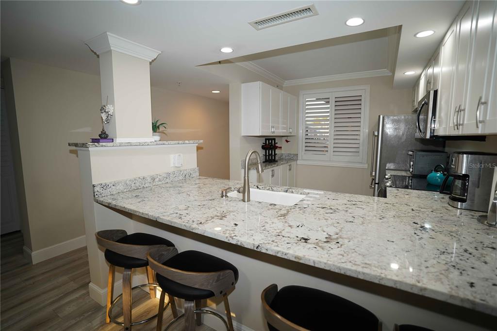 A kitchen features white cabinets, granite countertops, a breakfast bar, and three bar stools — 2101 MARINA ISLE WAY UNIT 104, JUPITER, FL