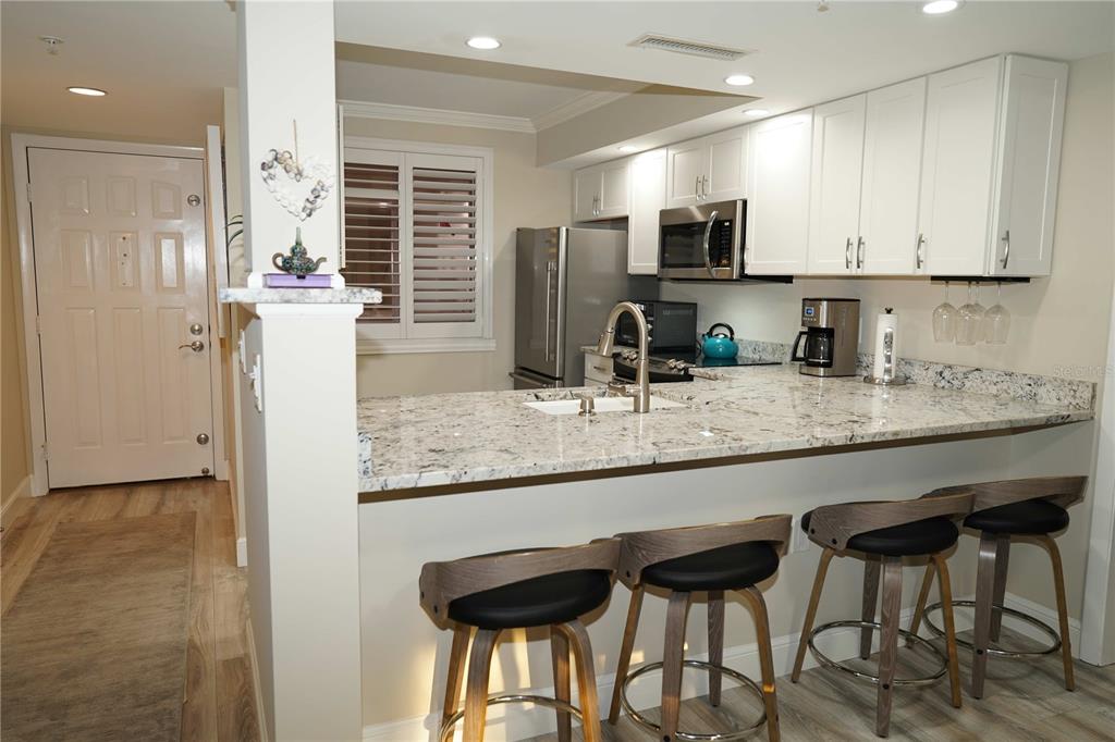 A kitchen features white cabinets, granite countertops, a breakfast bar with stools, and stainless appliances — 2101 MARINA ISLE WAY UNIT 104, JUPITER, FL