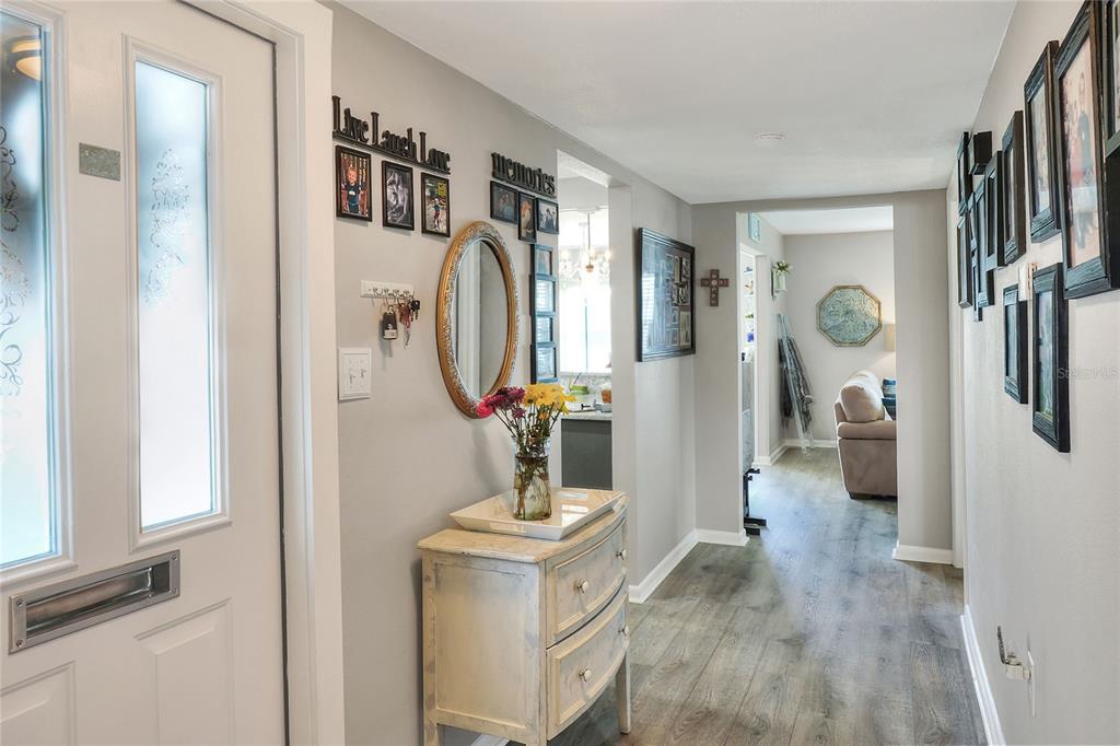An entryway features a white chest, a mirror, wall-mounted photos, and wood-look flooring — 3515 AMITY AVENUE UNIT 3515, LAKELAND, FL
