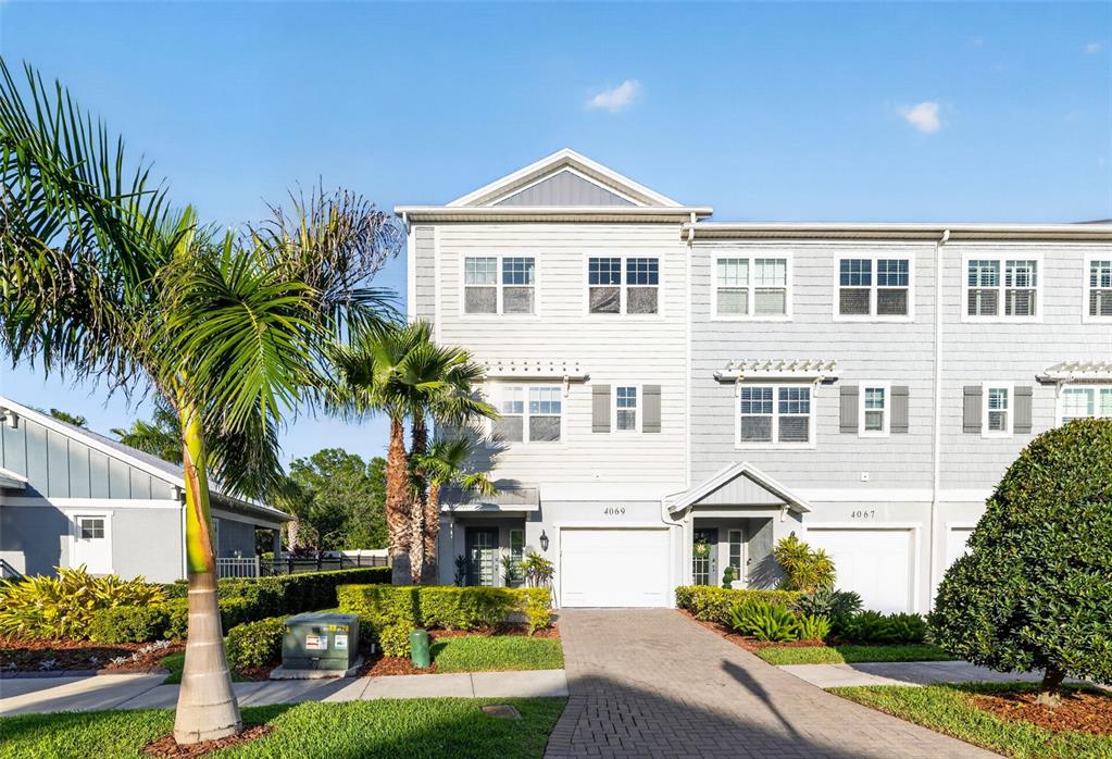 A three-story townhouse with light gray siding, a paved driveway, and palm trees in front — 4069 ROCKY SHORES DRIVE, TAMPA, FL