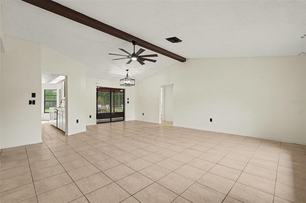 An open-concept living area features vaulted ceilings with exposed beams, tile flooring, and sliding doors — 4498 GONDOLIER RD, SPRING HILL, FL