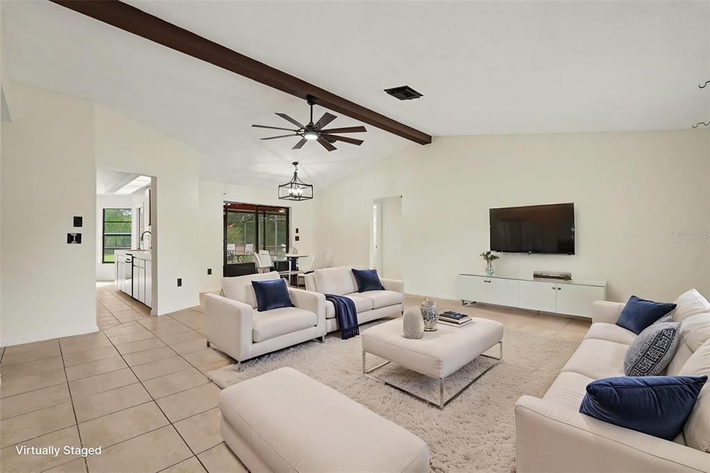 A living room with a vaulted ceiling, exposed beam, tile floors, and virtual furniture staging — 4498 GONDOLIER RD, SPRING HILL, FL