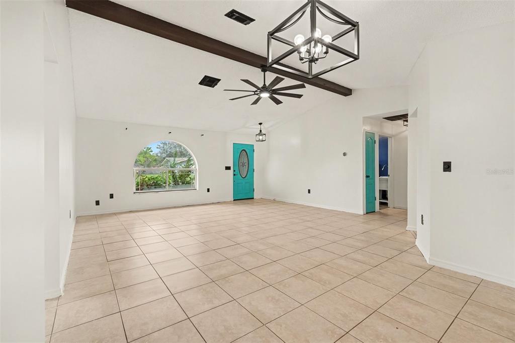 A bright living room features tile flooring, a vaulted ceiling with exposed beams, and a chandelier — 4498 GONDOLIER RD, SPRING HILL, FL