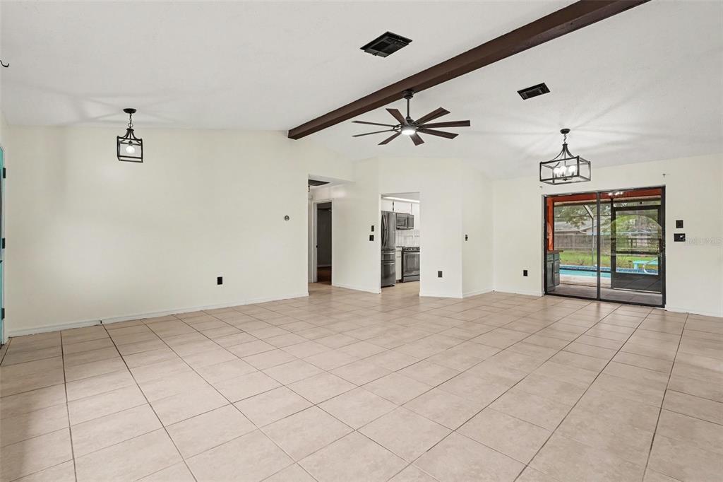 A spacious living room with tile flooring, a vaulted ceiling, and a sliding glass door — 4498 GONDOLIER RD, SPRING HILL, FL