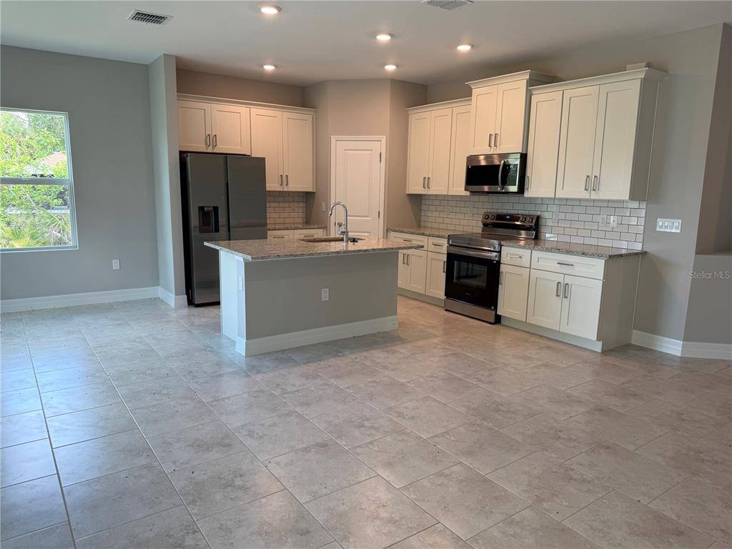 A kitchen features white cabinets, granite countertops, stainless steel appliances, and light tile flooring — 1275 PERRY STREET, PORT CHARLOTTE, FL