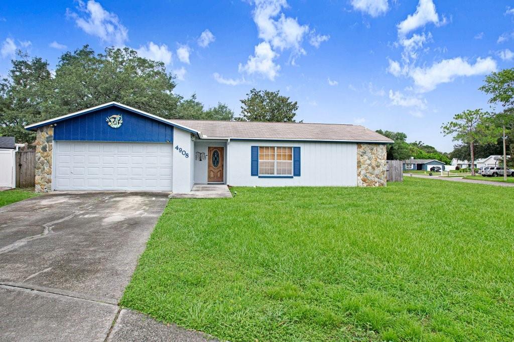 A single-story house with a white exterior, stone accents, a blue gable, and a concrete driveway — 4908 CROCKETT COURT, TAMPA, FL
