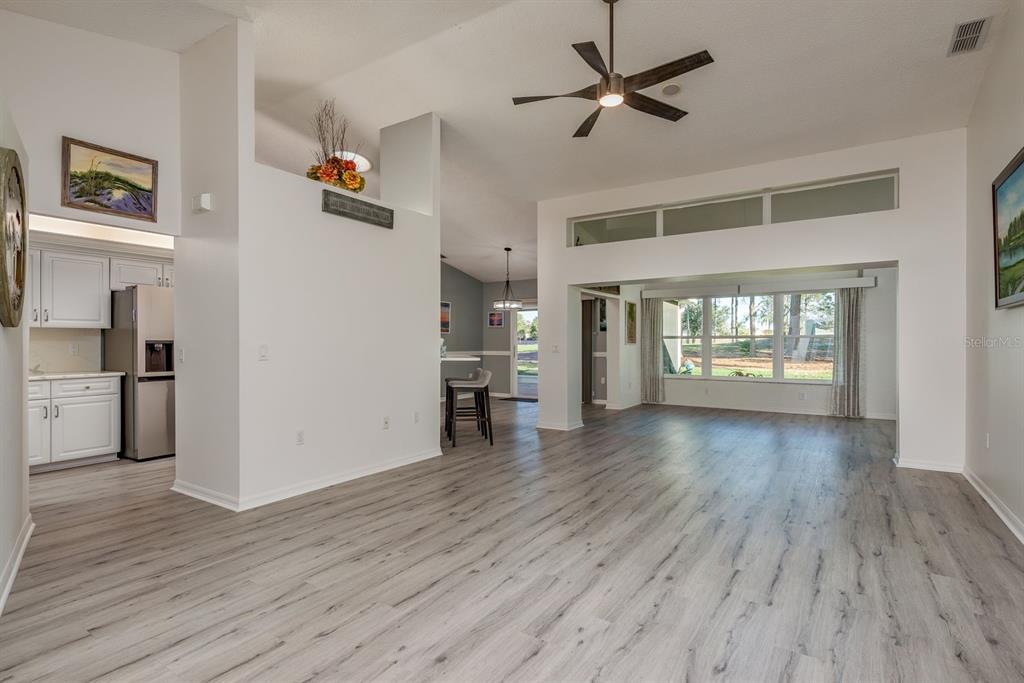 An open-concept living area with light wood-look flooring, a ceiling fan, and a kitchen corner — 9742 OAKWOOD HILLS COURT, NEW PORT RICHEY, FL