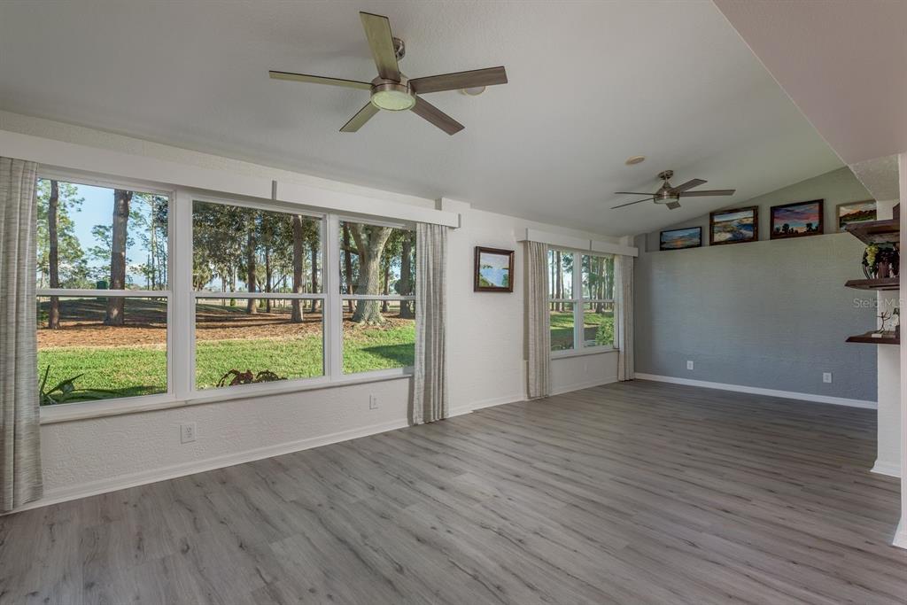 A bright living room features light wood-look flooring, large windows, and two ceiling fans — 9742 OAKWOOD HILLS COURT, NEW PORT RICHEY, FL