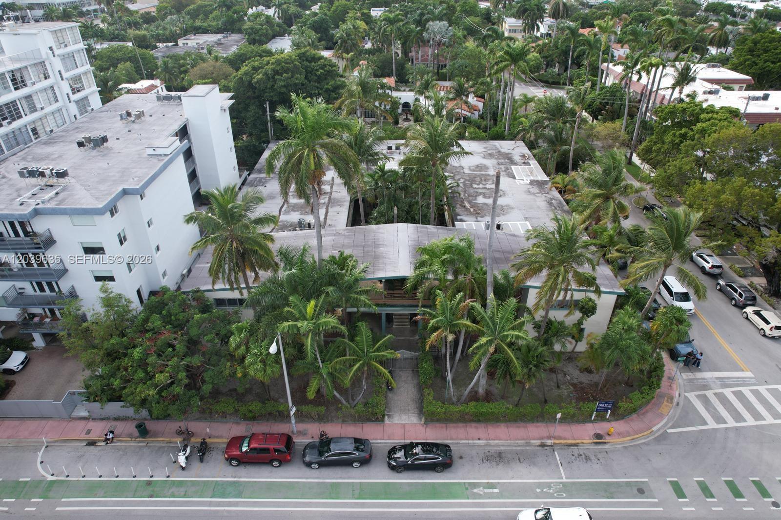 An aerial view shows a low-rise apartment building surrounded by palm trees and street parking — MIAMI BEACH, FL