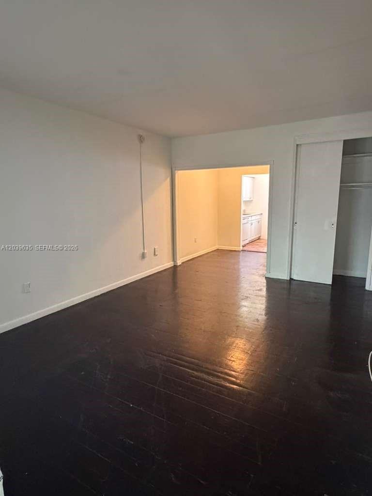 An empty room with dark wood floors leads to a kitchen through an open doorway — MIAMI BEACH, FL