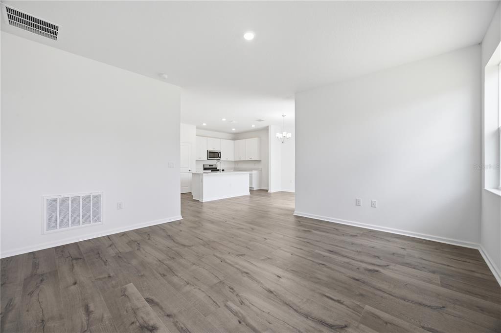 A bright, open-concept living area with wood-look flooring leads to a white kitchen — 5719 HIAWASSEE ROAD, OKAHUMPKA, FL