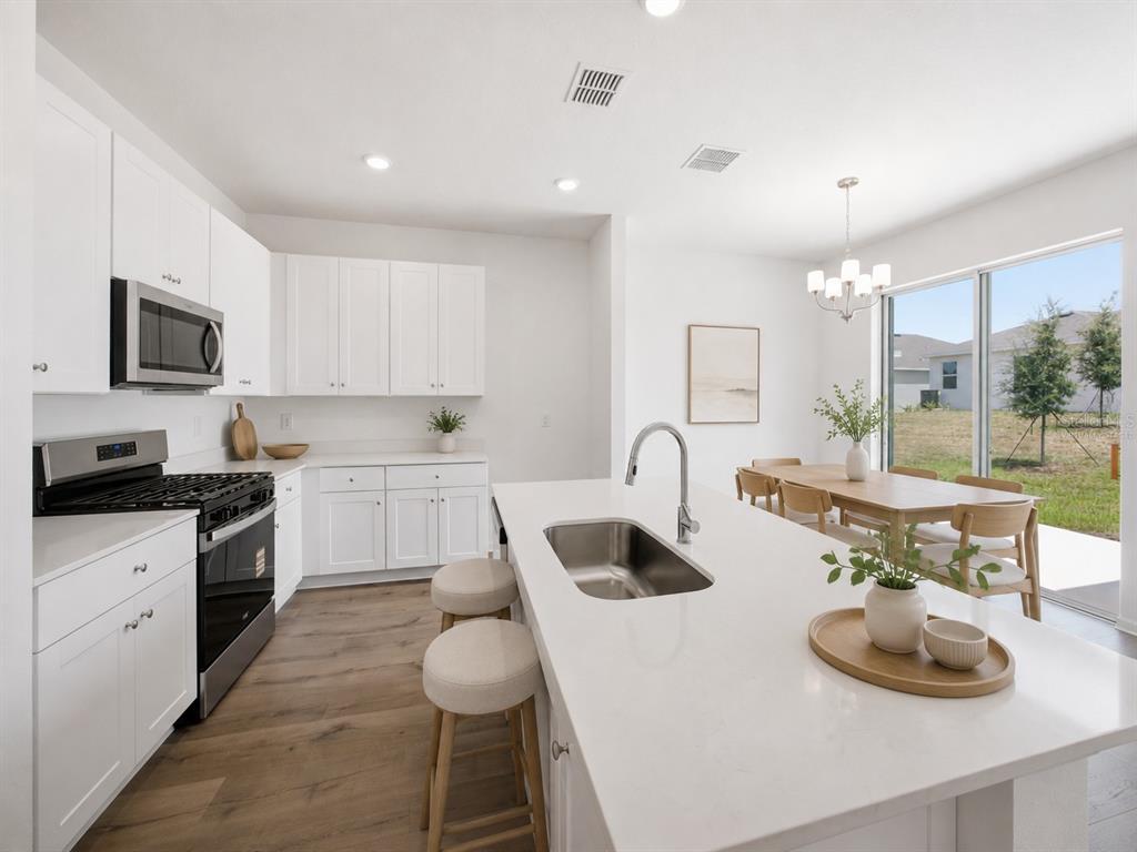 A modern kitchen features white cabinets, a quartz island with a sink, and dining area — 5719 HIAWASSEE ROAD, OKAHUMPKA, FL