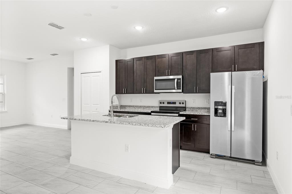 A kitchen with dark wood cabinets, granite countertops, stainless steel appliances, and light tile flooring — 9324 N FAIRY LILLY DR, CITRUS SPRINGS, FL
