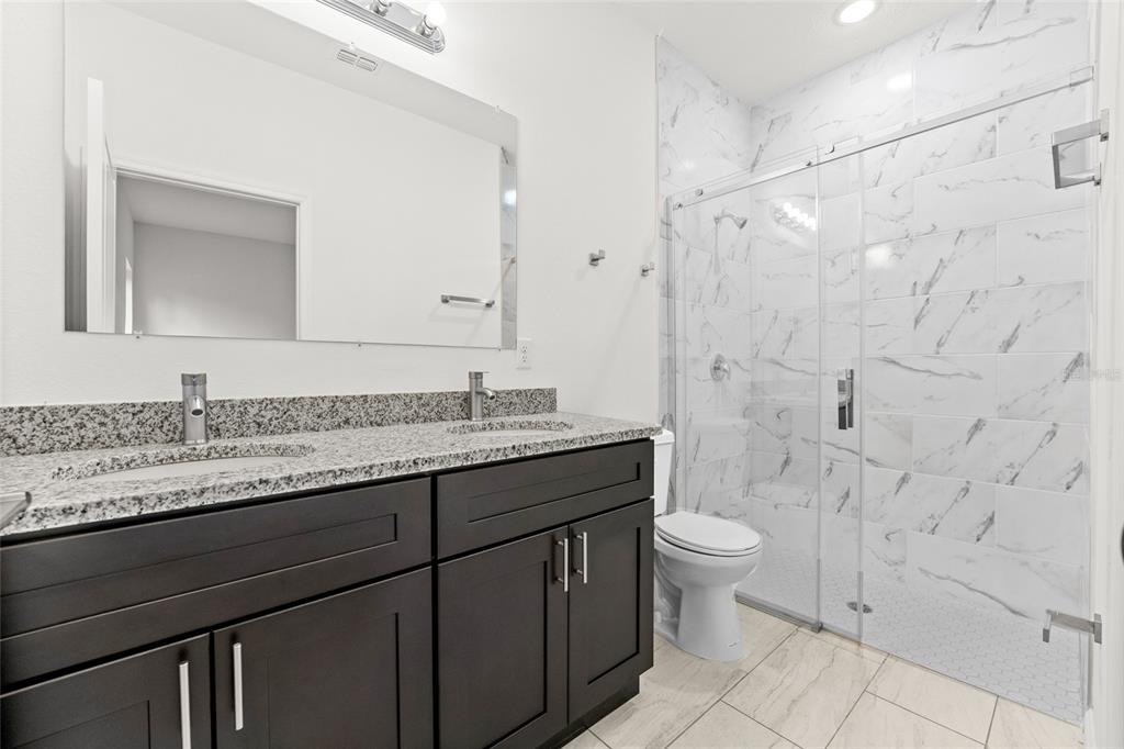 A bathroom features a double vanity with dark cabinets, granite countertops, and a glass-enclosed shower — 9324 N FAIRY LILLY DR, CITRUS SPRINGS, FL