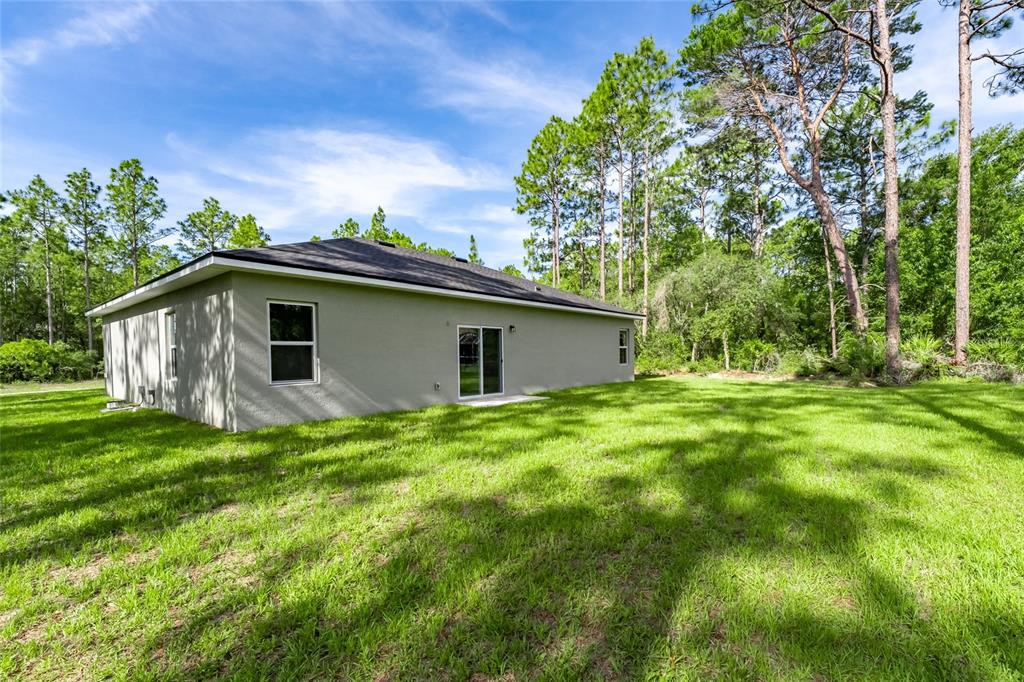 The exterior of a single-story house with a gray stucco finish and a grassy backyard — 9324 N FAIRY LILLY DR, CITRUS SPRINGS, FL