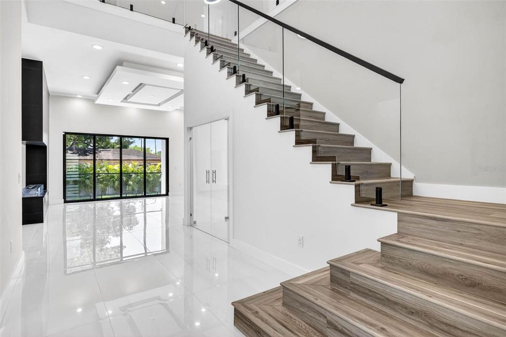 A modern foyer features white tile floors, a glass-railed staircase, and a large window wall — 4426 W EUCLID AVENUE, TAMPA, FL
