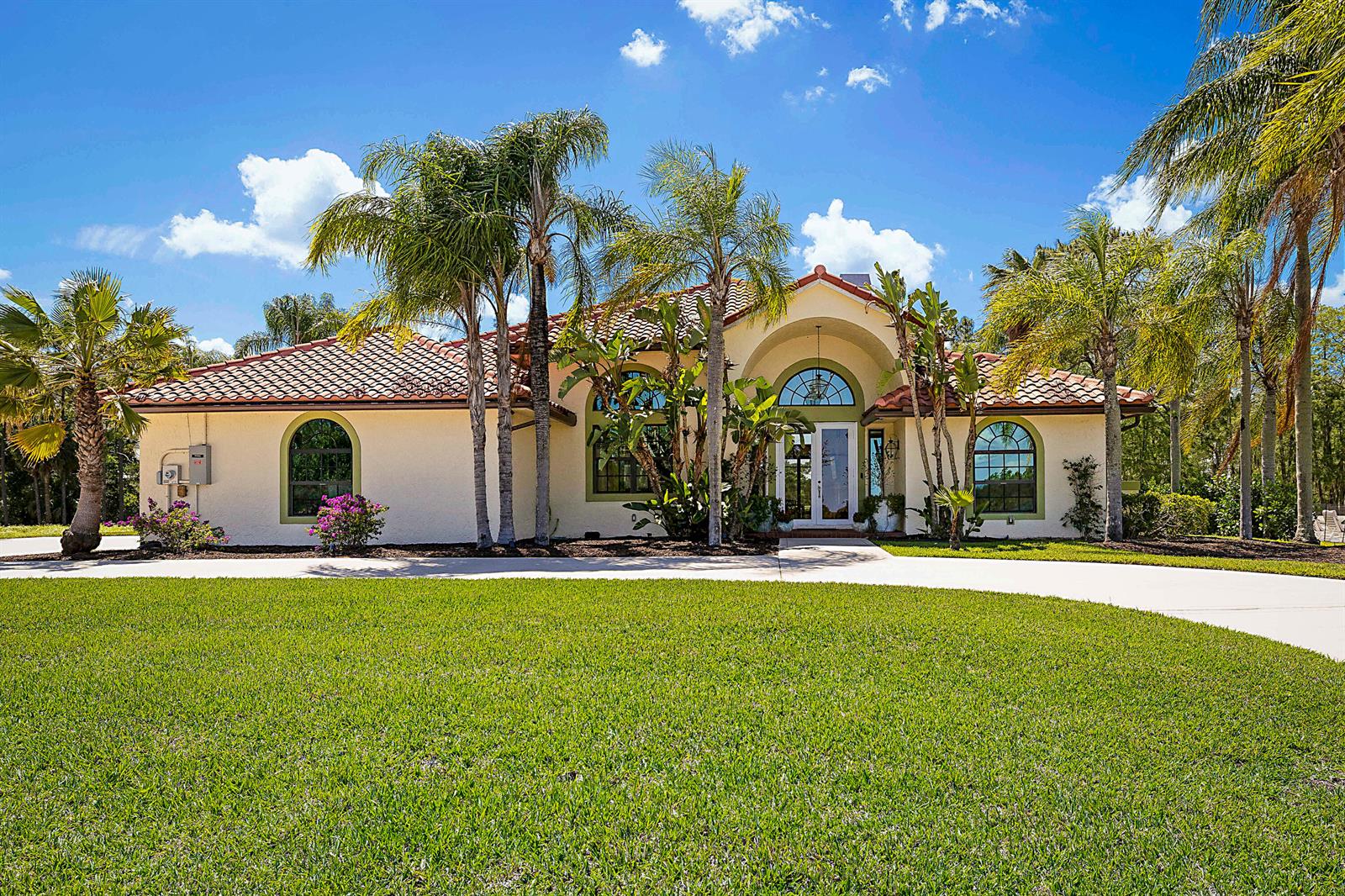 A single-story stucco house with a tile roof, arched windows, and palm trees in front — 18680 SE Old Trail Drive E, Jupiter FL 33478, JUPITER, FL