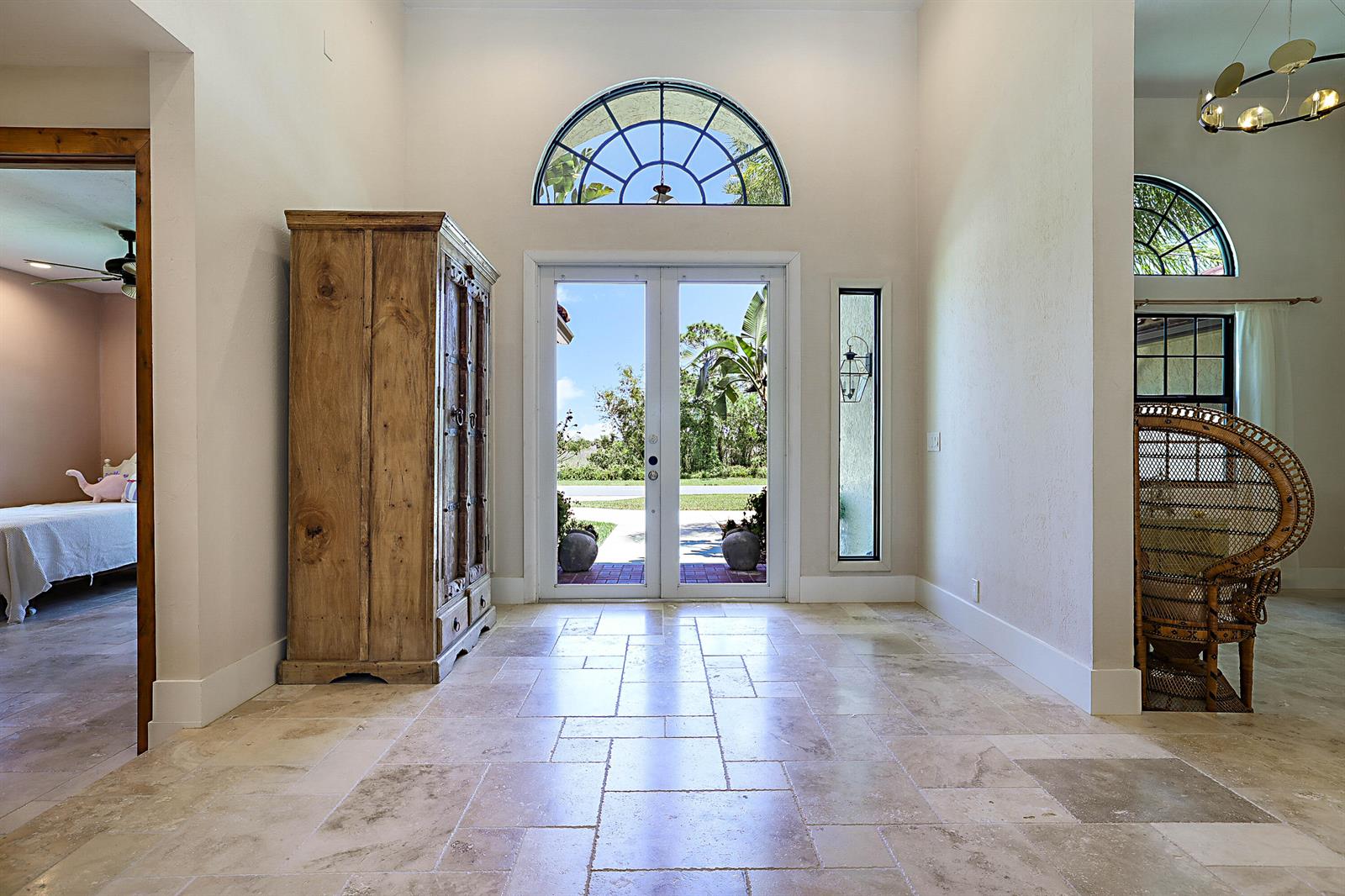 A bright entryway with stone tile flooring, a tall wooden cabinet, and double glass doors — 18680 SE Old Trail Drive E, Jupiter FL 33478, JUPITER, FL