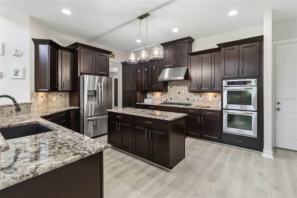 A kitchen features dark wood cabinetry, granite countertops, a center island, and light wood flooring — 9918 HATTON CIRCLE, ORLANDO, FL