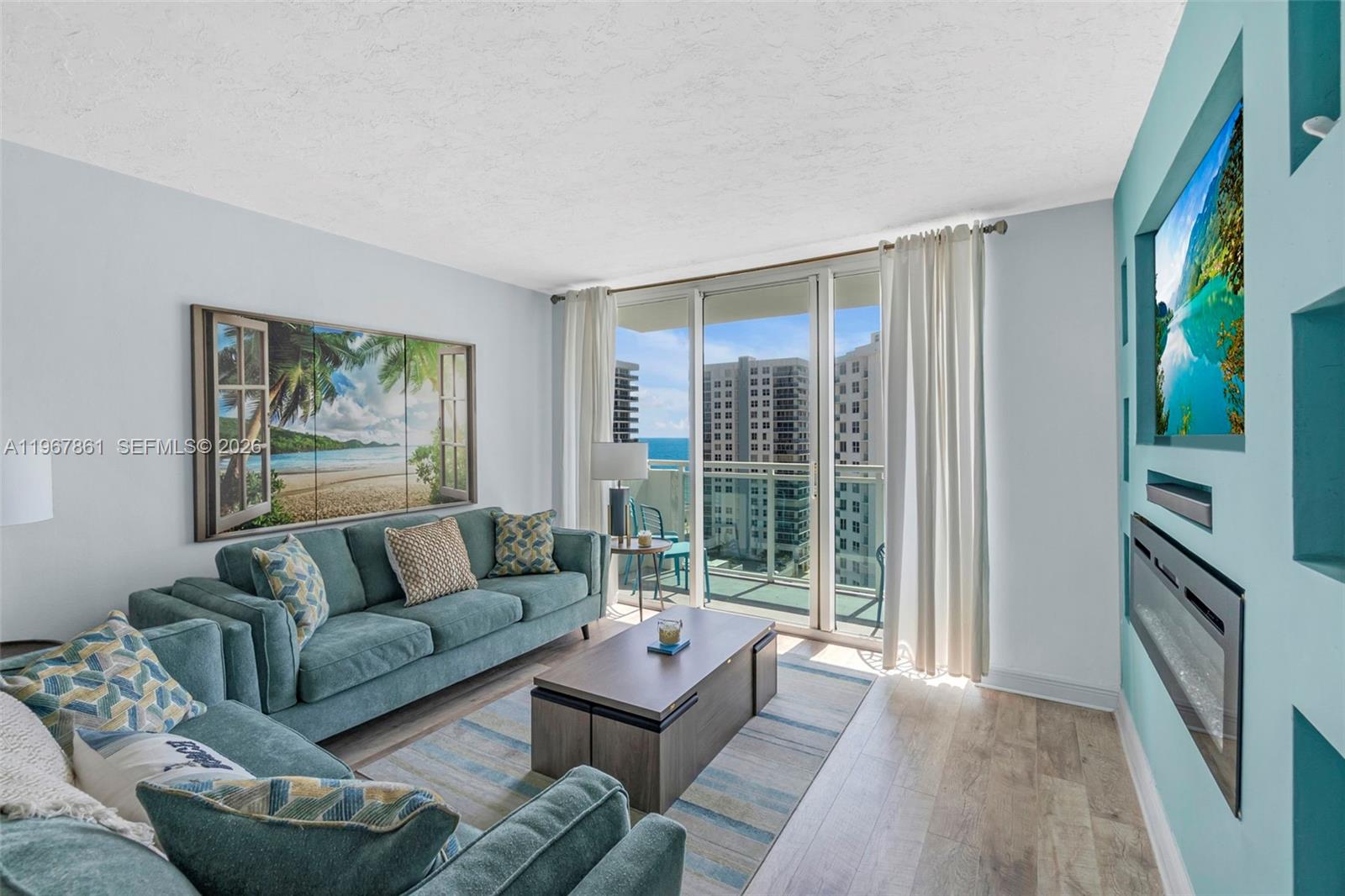 A living room features a blue sofa, a coffee table, and a balcony with ocean views — 3000 S Ocean Dr # 1122, Hollywood FL 33019, HOLLYWOOD, FL