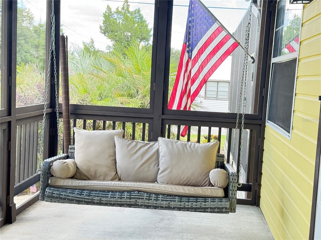 A gray wicker porch swing with beige cushions hangs on a screened-in porch — 398 VIRGINIA STREET, FROSTPROOF, FL