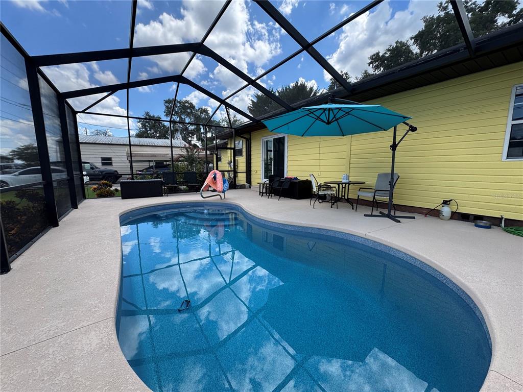 A swimming pool sits inside a screened-in patio next to a yellow house — 398 VIRGINIA STREET, FROSTPROOF, FL