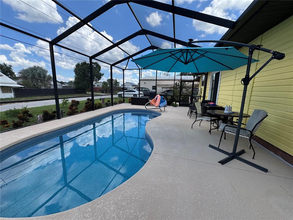A screened-in patio features a kidney-shaped swimming pool and a blue cantilever umbrella — 398 VIRGINIA STREET, FROSTPROOF, FL
