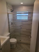 A bathroom features a glass-enclosed walk-in shower with light wood-look tile and a toilet — 189 Seville # 189, Delray Beach FL 33446, DELRAY BEACH, FL