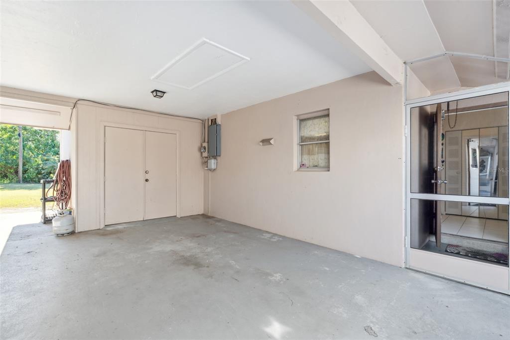 A covered concrete carport features a storage closet, an electrical panel, and a screened door — 235 THISTLE COURT, LEHIGH ACRES, FL