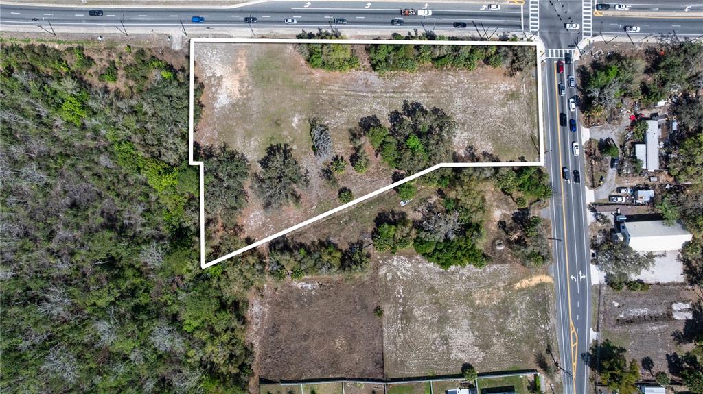 An aerial view shows a vacant, irregularly shaped lot bordered by a road and trees — 711 RONALD REAGAN PARKWAY, DAVENPORT, FL
