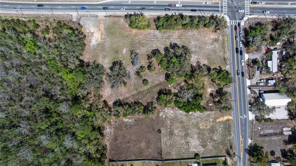 An aerial view shows a vacant, partially wooded lot situated at a road intersection — 711 RONALD REAGAN PARKWAY, DAVENPORT, FL